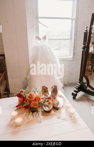 Hochzeitskleid am Fenster mit Blumenstrauß, Schuhen, Ringen und Kerzen Stockfoto