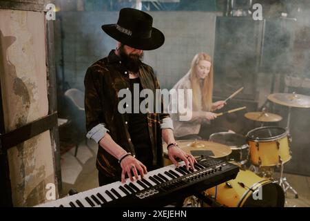 Bärtiger Musiker in stilvollem Outfit mit Hut, der Synthesizer in Rockband spielt, Kopierraum Stockfoto