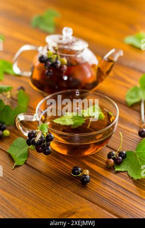 Kräutertee aus Johannisbeerblättern und Beeren in einer Tasse und in einer Teekanne, auf einem Holztisch Stockfoto