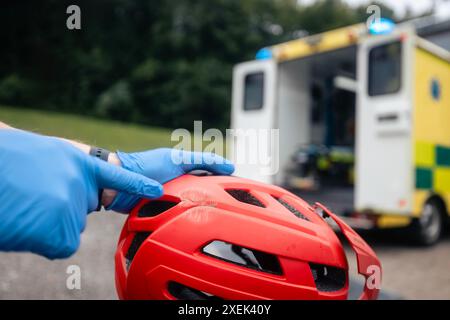 Rettungssanitäter zeigen an gebrochenem Fahrradsicherheitshelm nach Sturzradfahrer gegen Rettungswagen des Rettungsdienstes. Stockfoto