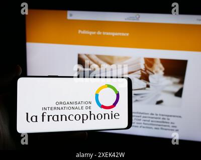 Person mit Smartphone und Logo der Organisation Internationale de la Francophonie vor der Website. Schwerpunkt auf dem Display des Telefons. Stockfoto