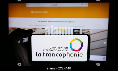 Person mit Handy und Logo der Organisation Internationale de la Francophonie vor der Webseite. Schwerpunkt auf dem Display des Telefons. Stockfoto