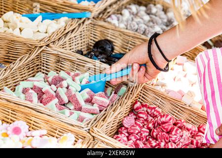 Nahaufnahme, detaillierte Ansicht einer weiblichen Hand, die rote, weiße und grüne Wassermelonenbonbons aus einem Korb, umgeben von einem Pick-and-Mix-Sortiment, schöpft Stockfoto