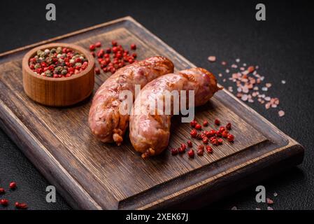 Köstliche gegrillte Hühnchen- oder Schweinefleisch-Würstchen mit Salz und Gewürzen auf dunklem Betonhintergrund Stockfoto