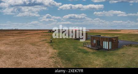 Blick aus der Vogelperspektive auf moderne Holzhütten im Grasfeld mit blauem Himmel Stockfoto