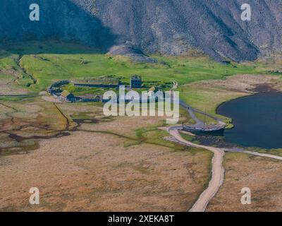 Aus der Vogelperspektive eines kleinen Dorfes mit Blick auf einen See in Islands Green Hills Stockfoto