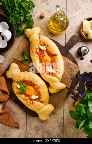 Khachapuri-Kuchen auf Ajarian. Offener Kuchen mit Käse und Ei auf Holzbrett mit Zutaten, Basilikum, Koriander, Eigelb und Gewürzen. Traditionelles georgisches c Stockfoto