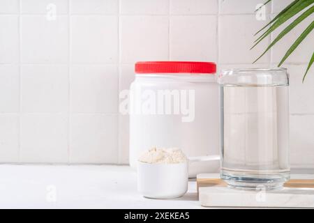 Kollagenproteinpulver mit Glas Wasser auf weißem Küchentisch. Natürliche Ergänzung für Schönheit, Gesundheit der Haut, Knochen, Gelenke und Darm, Anti Stockfoto