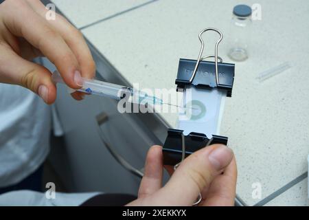 Herstellung von Kontaktlinsen. Arbeitshandschuhe füllen die Linsenform mit speziellem Amalgam mit einer Spritze. November 2018. Kiew, Ukraine Stockfoto