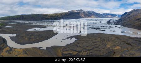 Blick aus der Vogelperspektive auf teilweise gefrorenen Gletschersee, umgeben von vulkanischem Felsen in Island Stockfoto