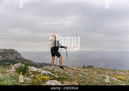 Eine Frau steht auf einem Hügel mit Blick auf das Meer. Sie hält einen Gehstock und genießt die Aussicht Stockfoto