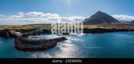 Blick aus der Vogelperspektive auf die felsige Küste und den kleinen Hafen in Island mit Bergkulisse Stockfoto