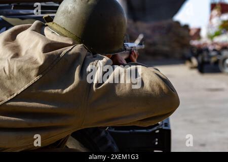 Nahaufnahme. Ein US-amerikanischer Infanterie-Soldat aus dem Zweiten Weltkrieg schießt während des Stadtkampfes hinter einem Militärfahrzeug. Blick von hinten Stockfoto
