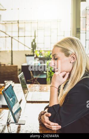 Zielgerichtete Geschäftsfrau analysiert Daten auf einem Laptop in einer modernen Büroumgebung. Sie engagiert sich in ihrer Arbeit mit einem nachdenklichen Ausdruck Stockfoto