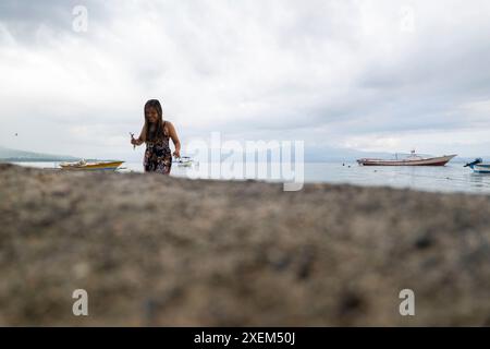 Frau genießt Zeit am Strand auf Bunaken Island, mit Booten, die im Wasser vor der Küste liegen, Nord-Sulawesi, Indonesien Stockfoto