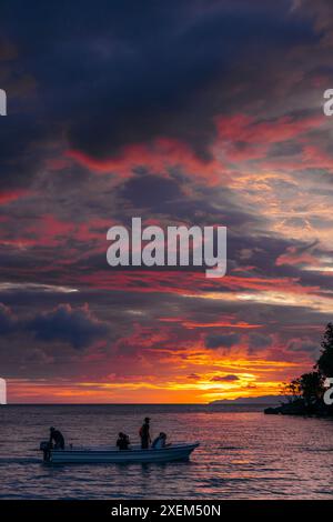 Bootstouren entlang der Küste der Insel Bolilanga bei Sonnenuntergang mit einem dramatischen, farbenfrohen Himmel auf den Togean-Inseln Indonesiens Stockfoto