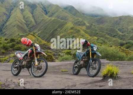 Motorräder mit Helmen, die auf dem Sand im Bromo Tengger Semeru Nationalpark geparkt sind, mit niedrigen, schweren Wolken über den Gipfeln des Tengger Massivs, Ost ... Stockfoto