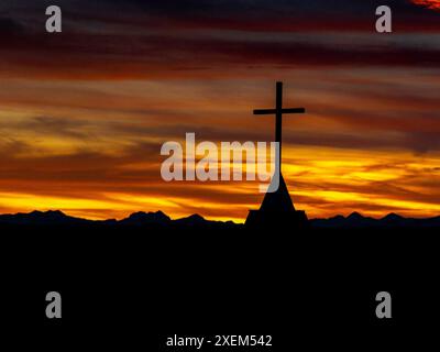 Silhouette eines Kirchturms vor einem dramatischen, farbenfrohen Himmel mit einer Silhouette von Bergen im Hintergrund; Calgary, Alberta, Kanada Stockfoto