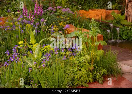 Iris sibirica „Persimmon“, Euphorbia und Digitalis purpurea neben Wasserrutschen im Octavia Hill Garden von Blue Diamond bei der Chelsea Flower Show Stockfoto