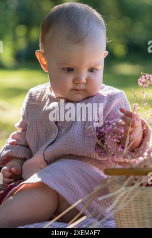 Porträt eines charmanten Babys in einem beigefarbenen Kleid. Das kleine Mädchen ist ein Jahr alt. Das Kind lächelt. Sonniger Tag auf der Par Stockfoto