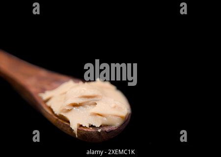Dieses Bild zeigt Nahaufnahme eines Holzlöffels mit Erdnussbutter auf schwarzem Hintergrund Stockfoto