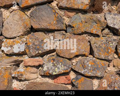 Eine Nahaufnahme einer alten Steinmauer. Die Steine sind verwittert und weisen Alterspuren auf, wobei Flechten auf ihrer Oberfläche wachsen. Stockfoto