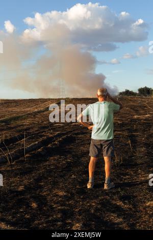 Ein Mann mit gedrehtem Rücken sieht nach dem Feuer besorgt auf sein verbranntes Feld aus. Er befindet sich rechts neben dem Bild. Vertikal. Stockfoto