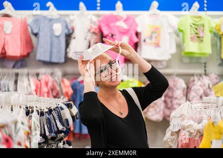 Eine schwangere Frau entscheidet, Kinderkleidung im Store. Stockfoto