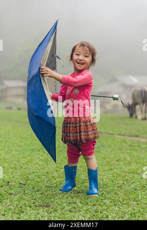 Mädchen spielt mit einem Regenschirm an einem regnerischen Tag in der Landschaft Vietnams; Ta so Village, MOC Chau District, Son La, Vietnam Stockfoto