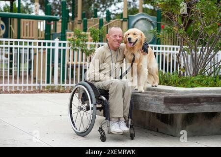 Informelles Porträt eines Mannes im Rollstuhl, der mit seinem Hund in einem Stadtpark Zeit verbringt; Bonynton Beach, Florida, Vereinigte Staaten von Amerika Stockfoto