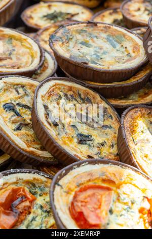 Leckeres vegetarisches Streetfood zum Mittagessen in London, verschiedene Quiche herzhafte Tarte mit Spinat, Tomaten, Pilzen, Cheddar-Käse, Nahaufnahme Stockfoto