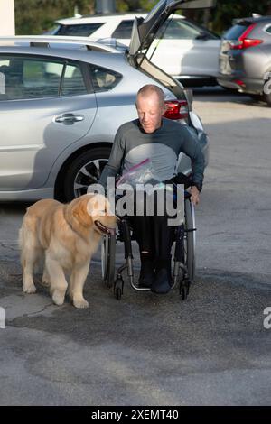 Querschnittsgelähmter in einem manuellen Rollstuhl und sein Diensthund auf einem Parkplatz; Boynton Beach, Florida, Vereinigte Staaten von Amerika Stockfoto