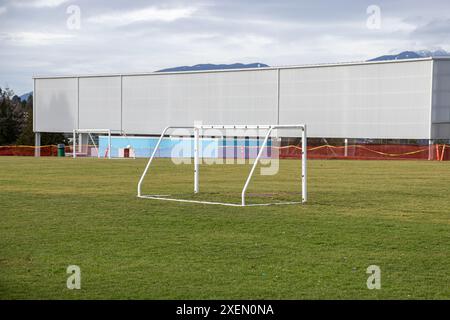 Leeres Fußballfeld (Fußballfeld) mit Metalltorpfosten auf grünem Gras, vor einem Hintergrund von Gebäuden und Bergen. Stockfoto