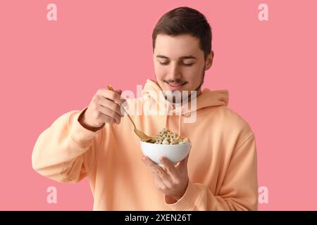 Schöner junger Mann, der leckere Müsliringe auf rosa Hintergrund isst Stockfoto