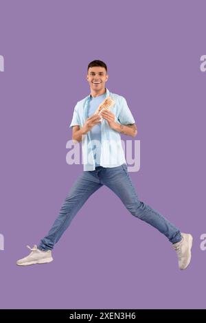 Springender junger Mann mit leckerem Döner-Kebab auf Fliederhintergrund Stockfoto