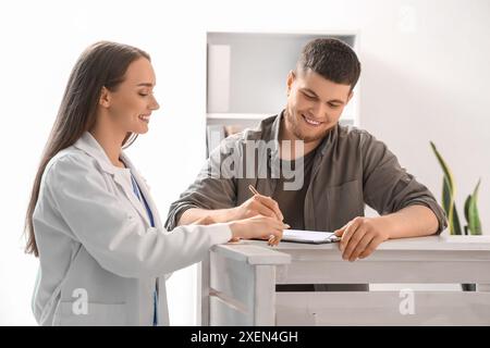 Weibliche Rezeptionistin mit Patienten, die das Formular im Krankenhaus ausfüllen Stockfoto