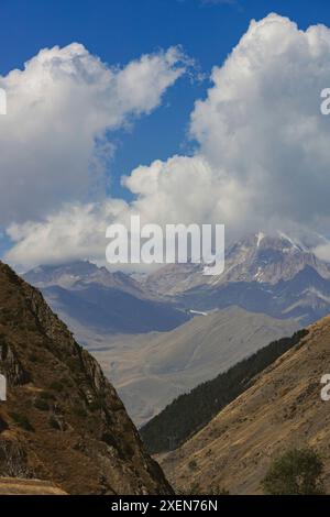 Blick durch Berghänge zu den Gipfeln des Kaukasus unter wehenden Kumulus-Wolken und einem blauen Himmel im Kazbegi Nationalpark in t... Stockfoto