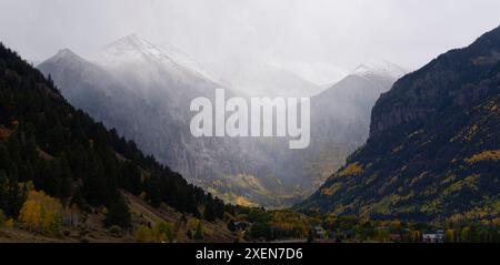 Malerischer Blick durch herbstfarbene Berghänge mit schneebedeckten Berggipfeln, die von Nebel bedeckt sind; in der Nähe von Aspen, Colorado, USA Stockfoto