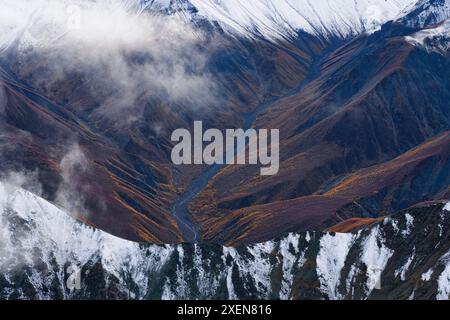 Aus der Vogelperspektive auf einen Fluss, der durch die herbstfarbenen Berghänge fließt, und die schneebedeckten Bergrücken des Kluane National Park, aufgenommen während der Reise... Stockfoto