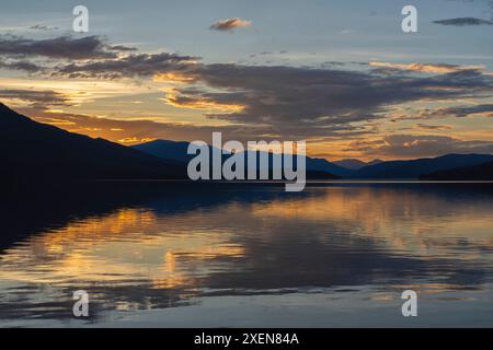 Sonnenuntergang über dem ruhigen See im Yukon, mit silbrigen Bergen und leuchtenden Wolken, die sich im ruhigen Wasser spiegeln; Yukon, Kanada Stockfoto
