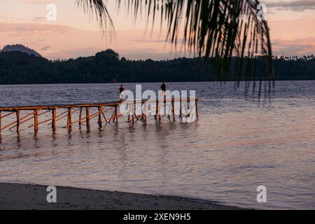 Jungs laufen bei Sonnenuntergang in einem Resort auf der Insel Bolilanga auf den togischen Inseln Indonesiens bis zum Ende eines Docks Stockfoto