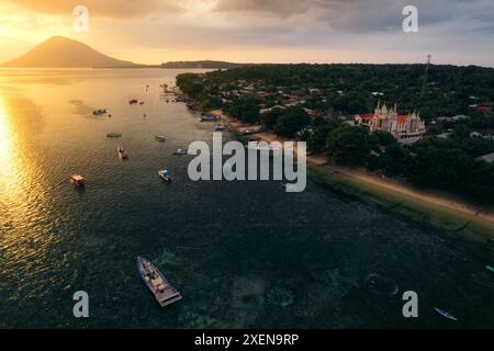 Boote vor der Küste von Bunaken bei Sonnenuntergang mit Blick auf die Kirche und Manado Tua im Hintergrund, Nord-Sulawesi, Indonesien Stockfoto