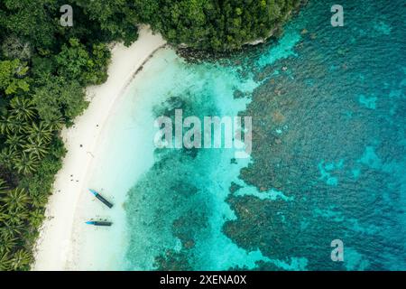 Boote am Ufer eines weißen Sandstrandes im Kepulauan Togean National Park, mit einem Riff durch das klare türkisfarbene Meer Stockfoto