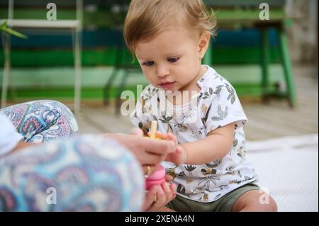 Kaukasischer kleiner Junge zeigt Interesse, während er eine lehrreiche bunte Pyramide aus Öko-Holz zusammenbaut. Das Konzept der Lernspiele für ch Stockfoto