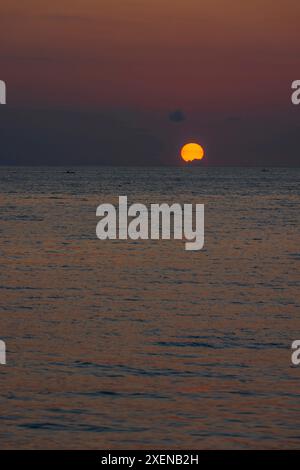 Dramatisch glühende Sonne, die über dem Meer mit kleinen Booten im ruhigen Wasser in Zentral-Sulawesi, Indonesien, untergeht Stockfoto