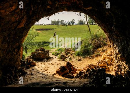 Sie blicken von einem Höhleneingang auf Touristen, die in der archäologischen Weltkulturerbestätte Plain of Jars Site 1 in Phonsavan, Laos, stehen Stockfoto