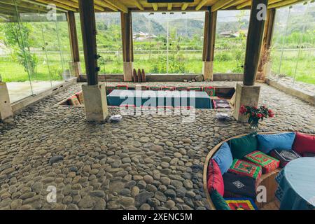 Versenkte Sitzbereiche mit bunten Kissen in einem Raum mit Glaswänden für natürliches Licht; Ngoc Chien, Muong La District, Son La, Vietnam Stockfoto