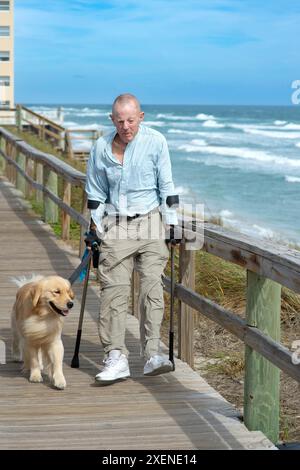 Querschnittsgelähmter mit Unterarmkrücken und Begleithund spazieren gern entlang der Meerespromenade; Boynton Beach, Florida, Vereinigte Staaten von Amerika Stockfoto