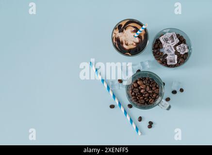 Tasse Eiskaffee, Kaffeetassen voller gerösteter Kaffeebohnen und Eiswürfel und Papierstroh auf pastellblauem Hintergrund. Minimales kreatives Sommerkonzept Stockfoto