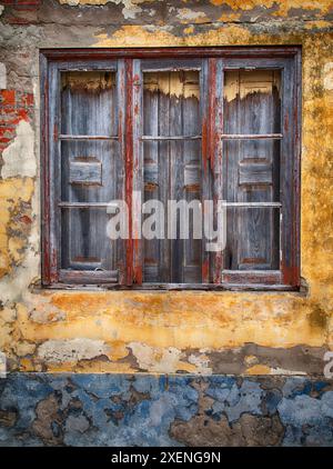 Portugal, Costa Nova. Sehr altes Holzfenster mit Fensterläden an einer bunten Wand mit abblätternder Farbe. Stockfoto
